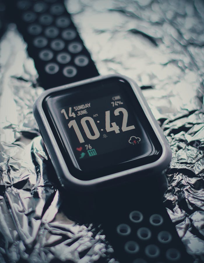 Stylish black smartwatch with digital display showing time and date on shiny foil background.