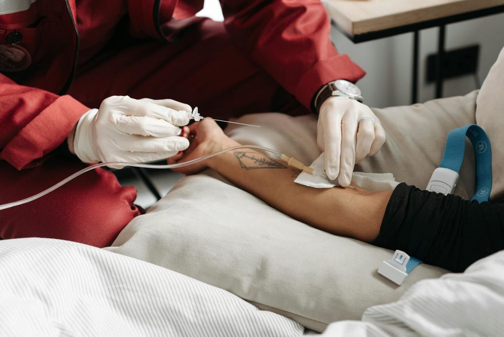 Paramedic in red uniform giving IV treatment to patient at home setting.